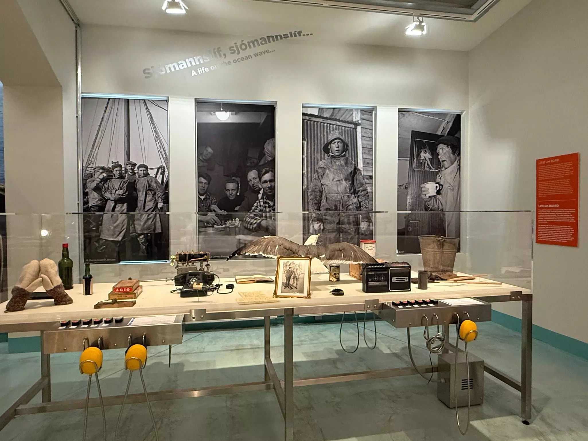 A display in a museum has various objects in a glass box with photographs of fishers in full fishing gear on the walls.