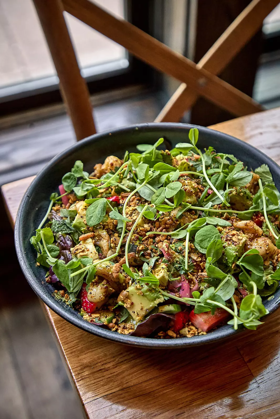 A bowl of salad with strawberries, avocado, greens and other items.