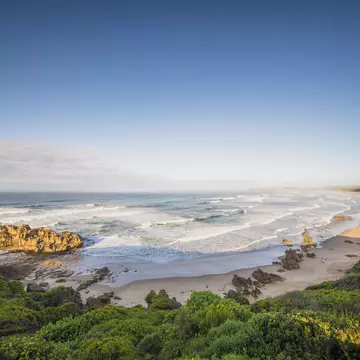 A long curve of sand backed by lush hills is pounded by waves.