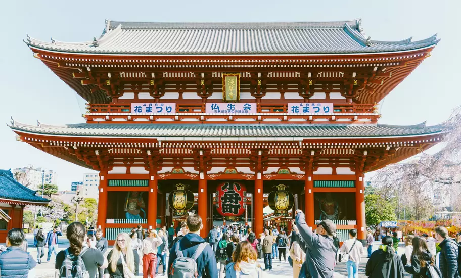 Crowds of people gather in the square in front of a red-roofed temple, Sensō-ji in Tokyo, Japan. 