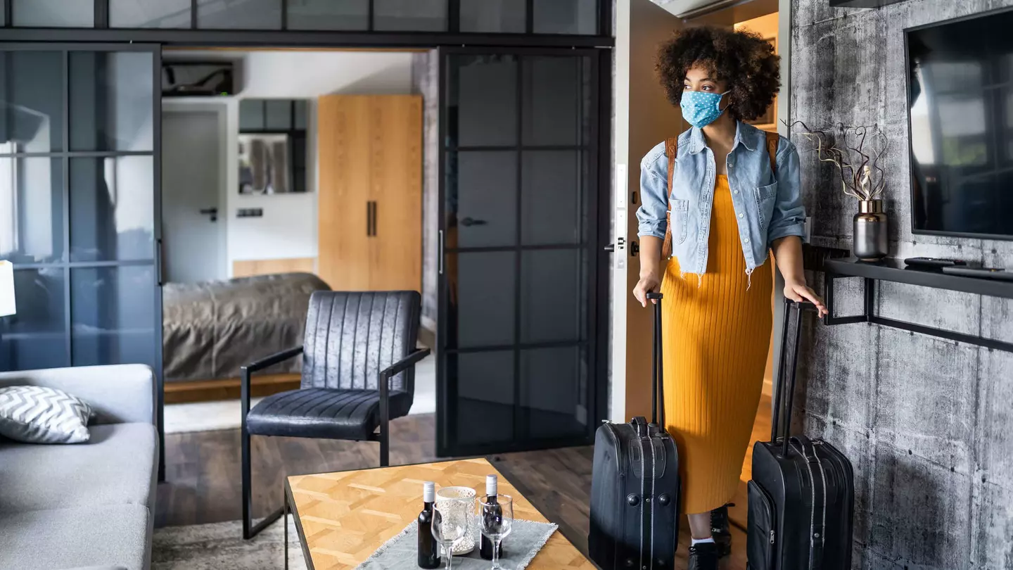 Woman with protective face mask arriving in hotel room.