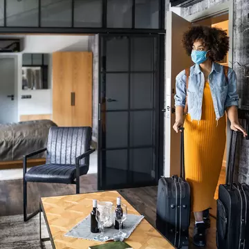 Woman with protective face mask arriving in hotel room.