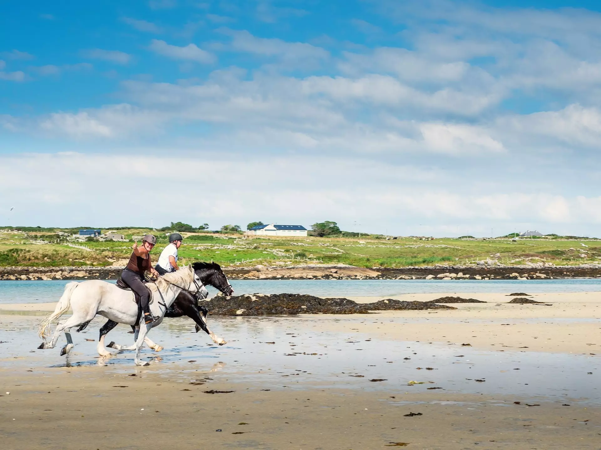 Omeye island, county Galway, Ireland : Couple riding horses on Omey beach, warm sunny day. Outdoor activity and fun concept. Women shows thumbs up. Black and white stunning horses., License Type: media, Download Time: 2025-12-04T16:25:03.000Z, User: nic.dhoedt_lonelyplanet, Editorial: true, purchase_order: 56530 - Guidebooks, job: Global Publishing WIP , client: Lonely Planet Ireland 17, other: Nicolas D'hoedt