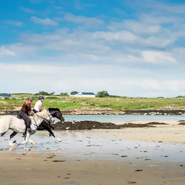 Omeye island, county Galway, Ireland : Couple riding horses on Omey beach, warm sunny day. Outdoor activity and fun concept. Women shows thumbs up. Black and white stunning horses., License Type: media, Download Time: 2025-12-04T16:25:03.000Z, User: nic.dhoedt_lonelyplanet, Editorial: true, purchase_order: 56530 - Guidebooks, job: Global Publishing WIP , client: Lonely Planet Ireland 17, other: Nicolas D'hoedt