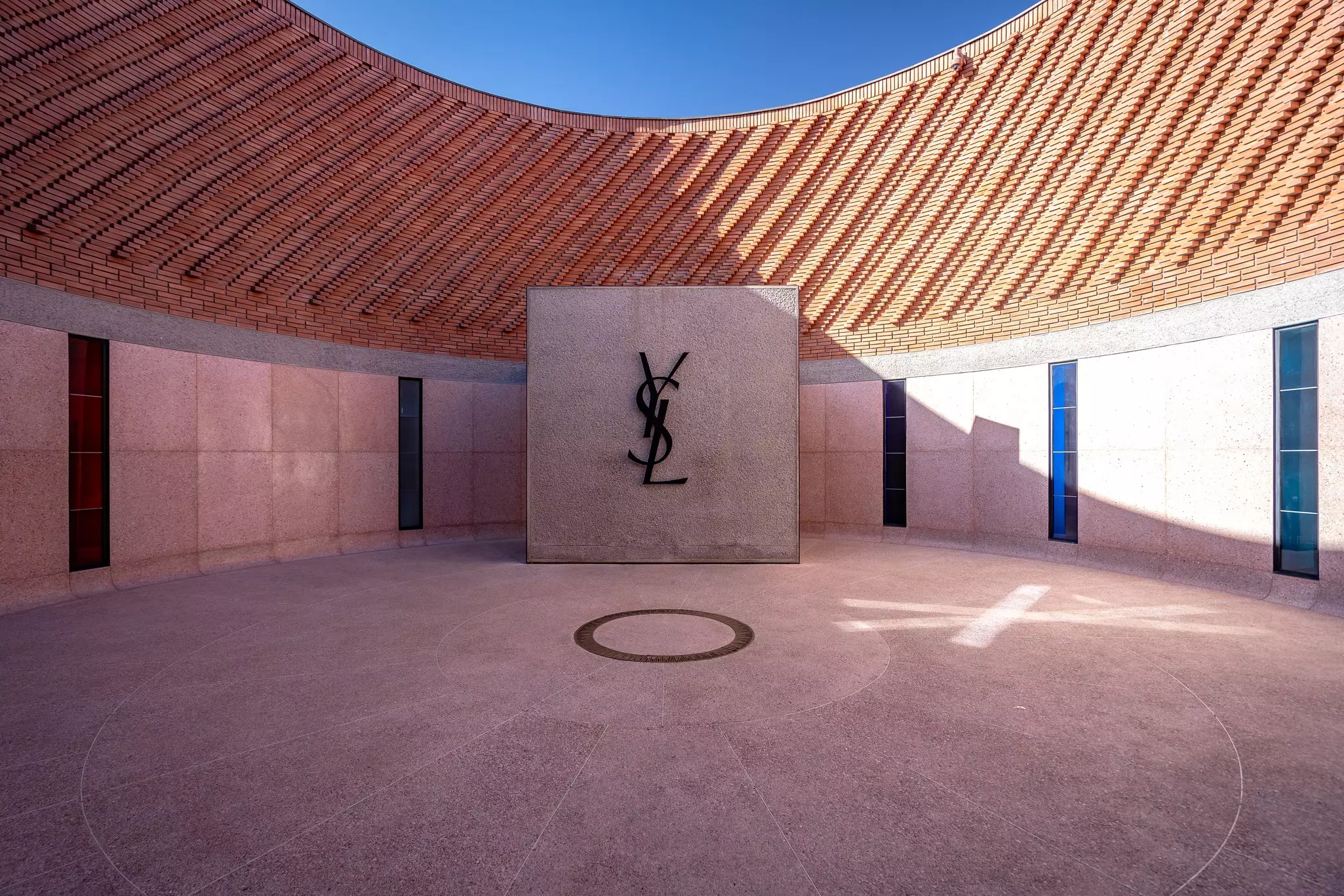 A central circular courtyard of a museum with a large logo on a wall comprising of overlapping letters: YSL