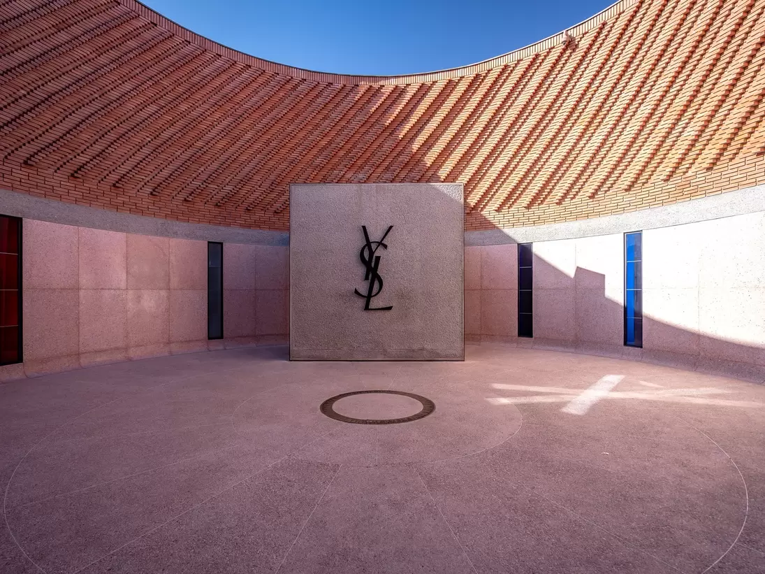 A central circular courtyard of a museum with a large logo on a wall comprising of overlapping letters: YSL