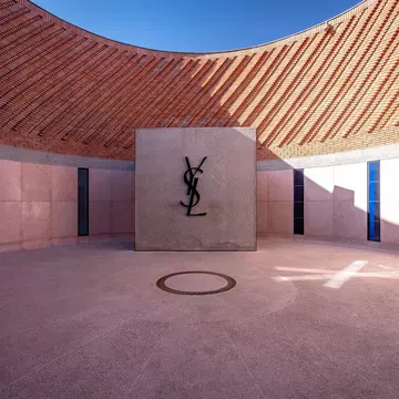 A central circular courtyard of a museum with a large logo on a wall comprising of overlapping letters: YSL