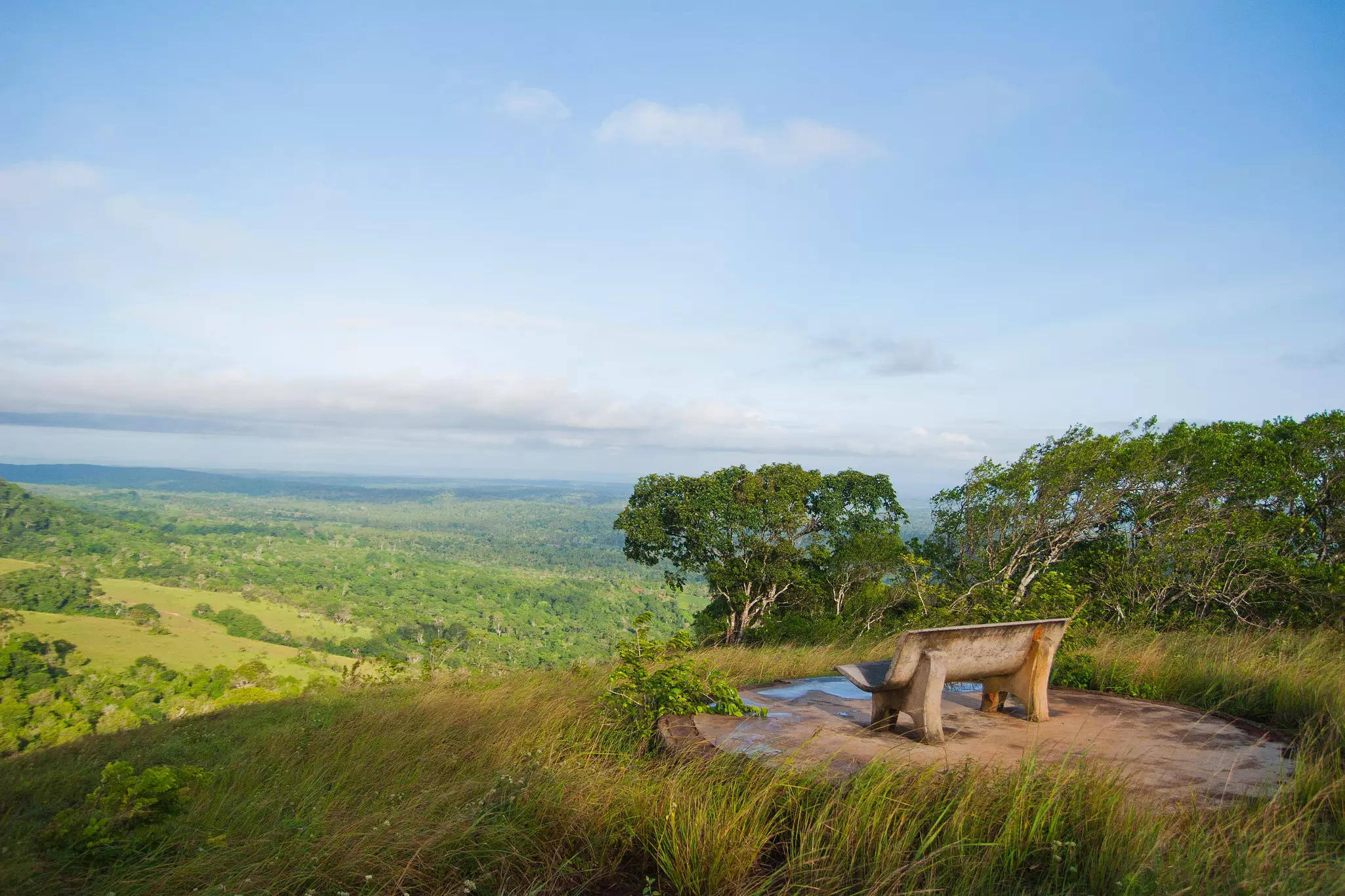 Two Maasai in traditional attire (flowing red, orange and blue robes) stand on rocks, with the grassy savannah and Mt Kilimanjaro as a backdrop.