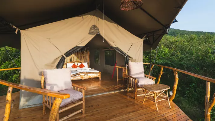 Sun shines onto the double bed in a tented room on a wooden deck