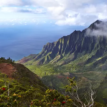 Looking down a green valley with jagged cliffs on the Nāpali Coast in Kauaʻi, Hawaii.