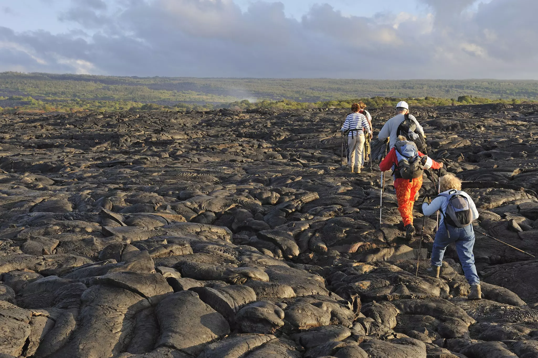 Group of hikers walking on cooled pahoehoe lava flow at sunrise, Kilauea Volcano, Big Island, Hawaii Islands, USA