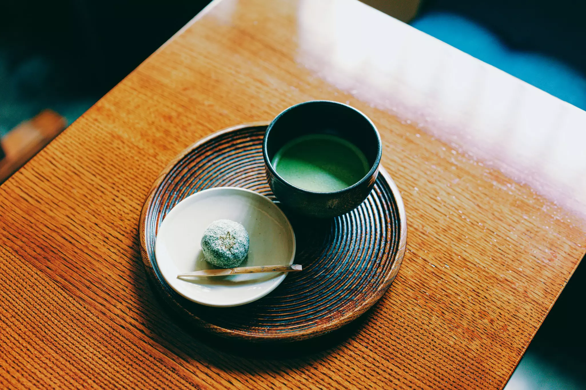 Green tea served in a bowl that's placed on a plate on a table with a small snack on a plate beside it
