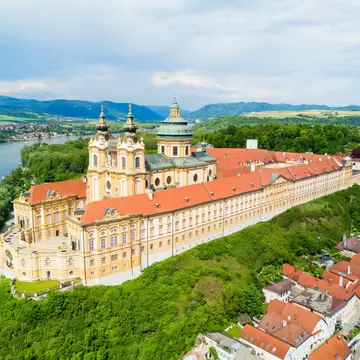 Melk Abbey, Austria: twin-towered yellow baroque church and long red-roofed wings on a wooded bluff, Danube river behind