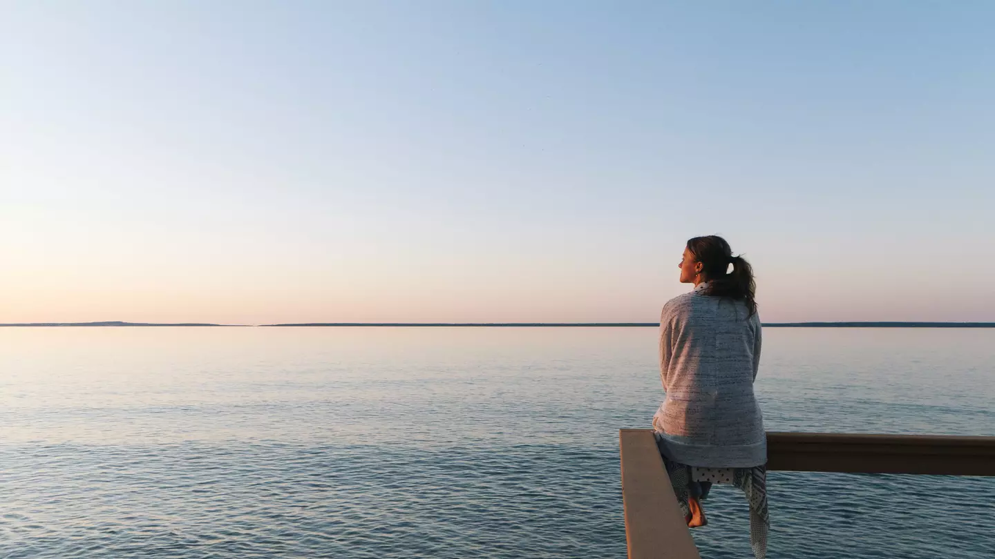 Young woman sitting on edge looks out at view of a lake