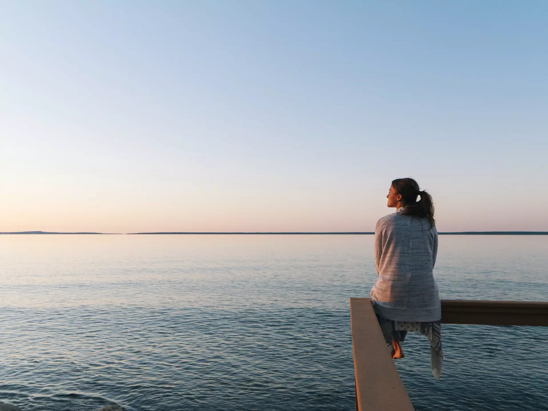 Young woman sitting on edge looks out at view of a lake