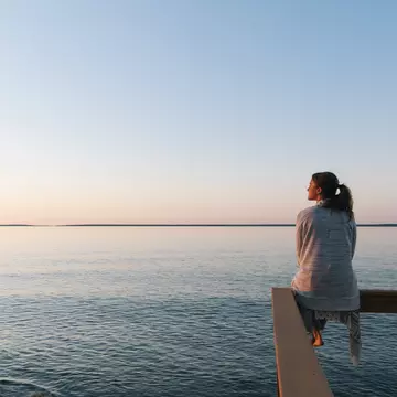 Young woman sitting on edge looks out at view of a lake