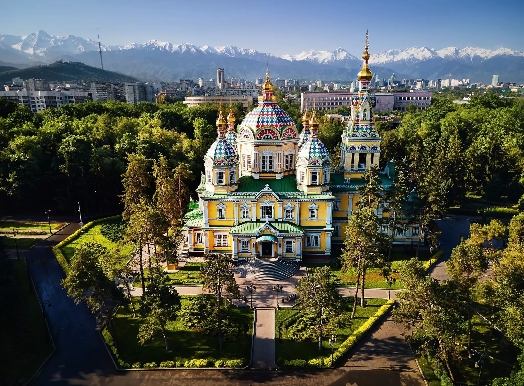 Trees surround the Ascension (Zenkov) Cathedral against a backdrop of mountains in Almaty, Kazakhstan.