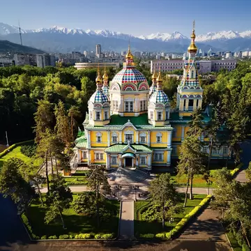 Trees surround the Ascension (Zenkov) Cathedral against a backdrop of mountains in Almaty, Kazakhstan.