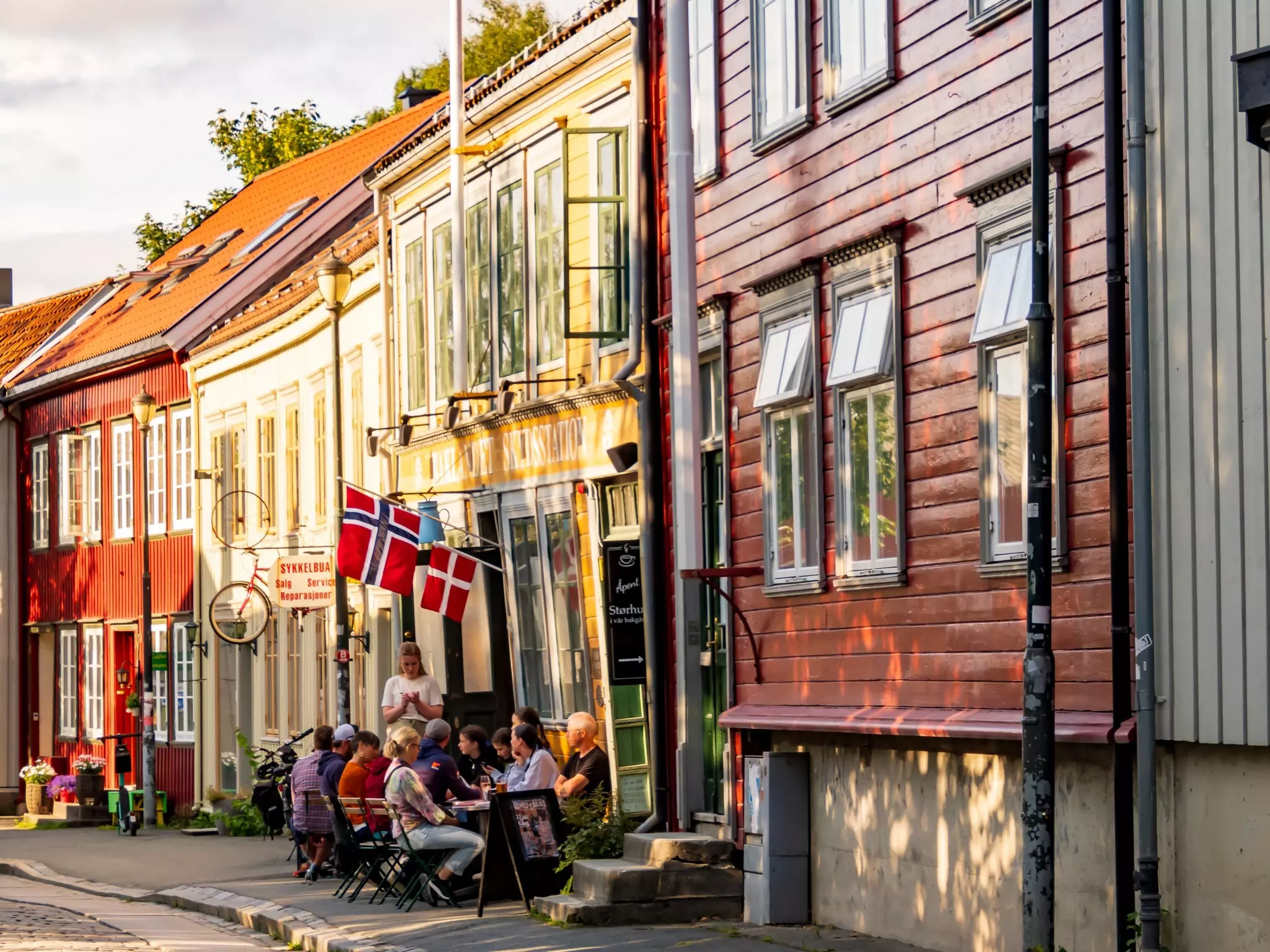 People sit at tables on a sidewalk on a city street with small, brightly painted houses.