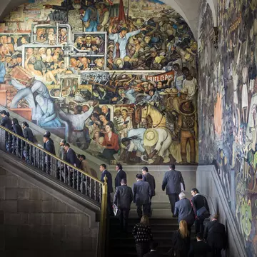 People walk up a staircase in front of a huge, elaborate, colorful mural.
