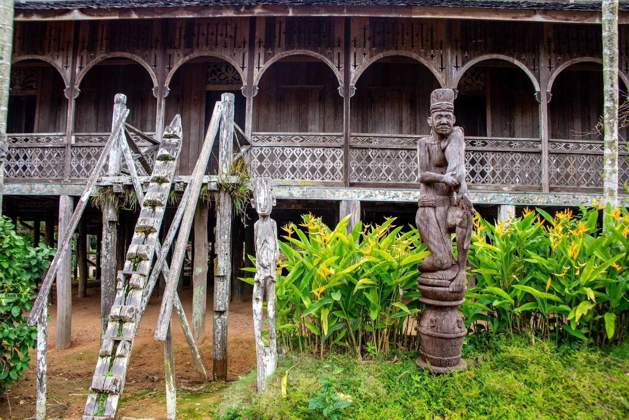 Carved wooden sculptures sit outside a wooden structure with a carved facade.