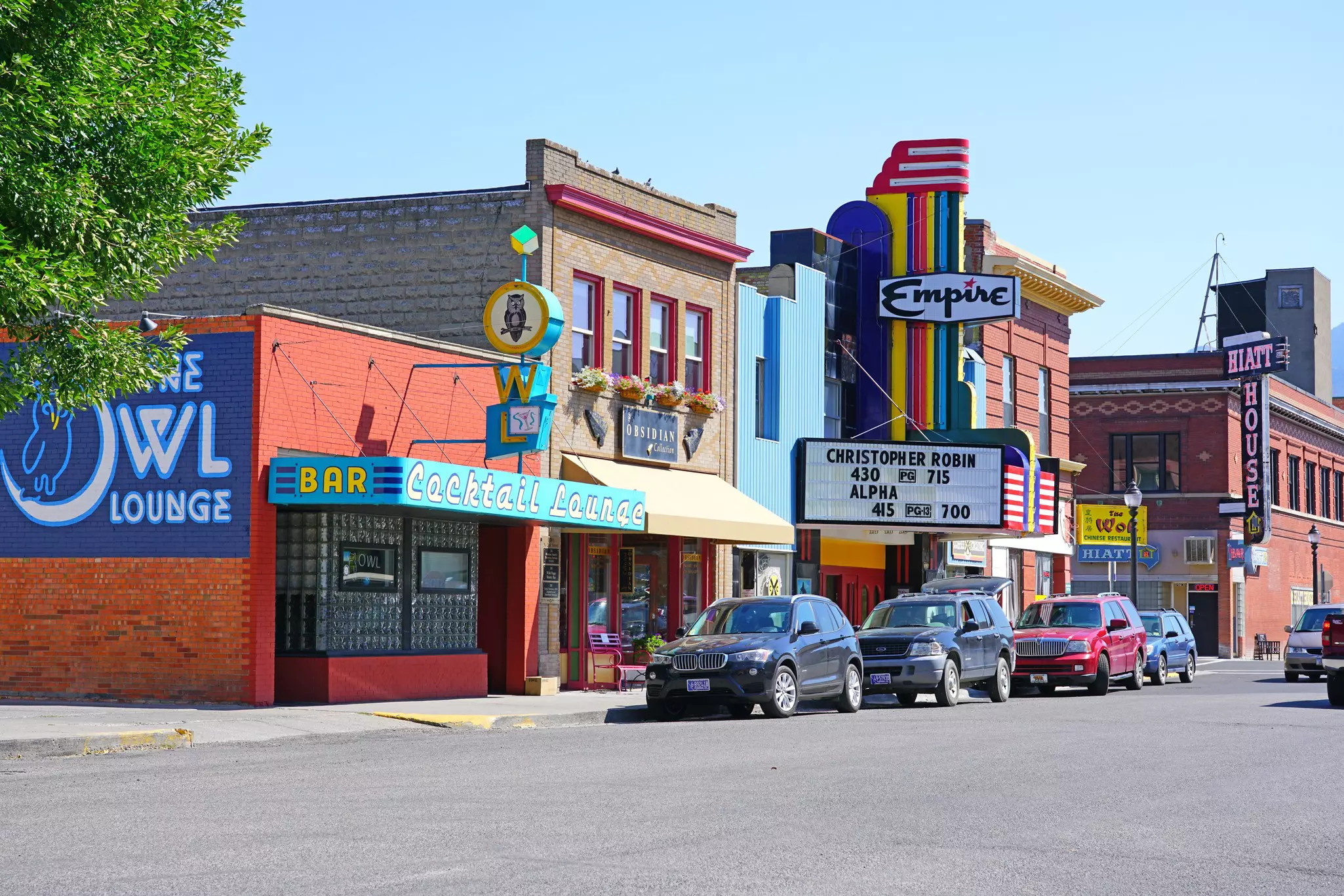 A street through a town with low-rise vuuldings and a corner bar with a large sign on the side that says "the Owl Lounge" and one of the front that says "bar cocktail lounge"