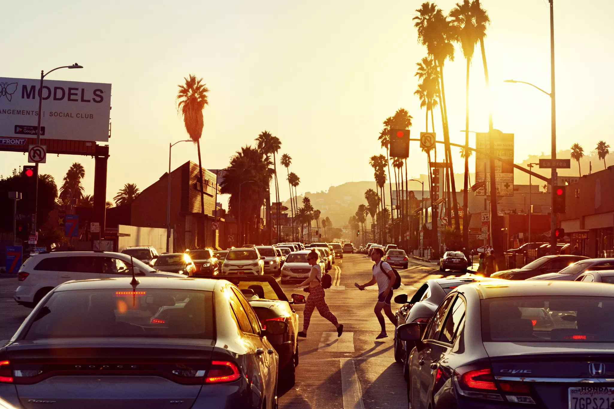 A couple of pedestrians cross a busy LA road at sunset