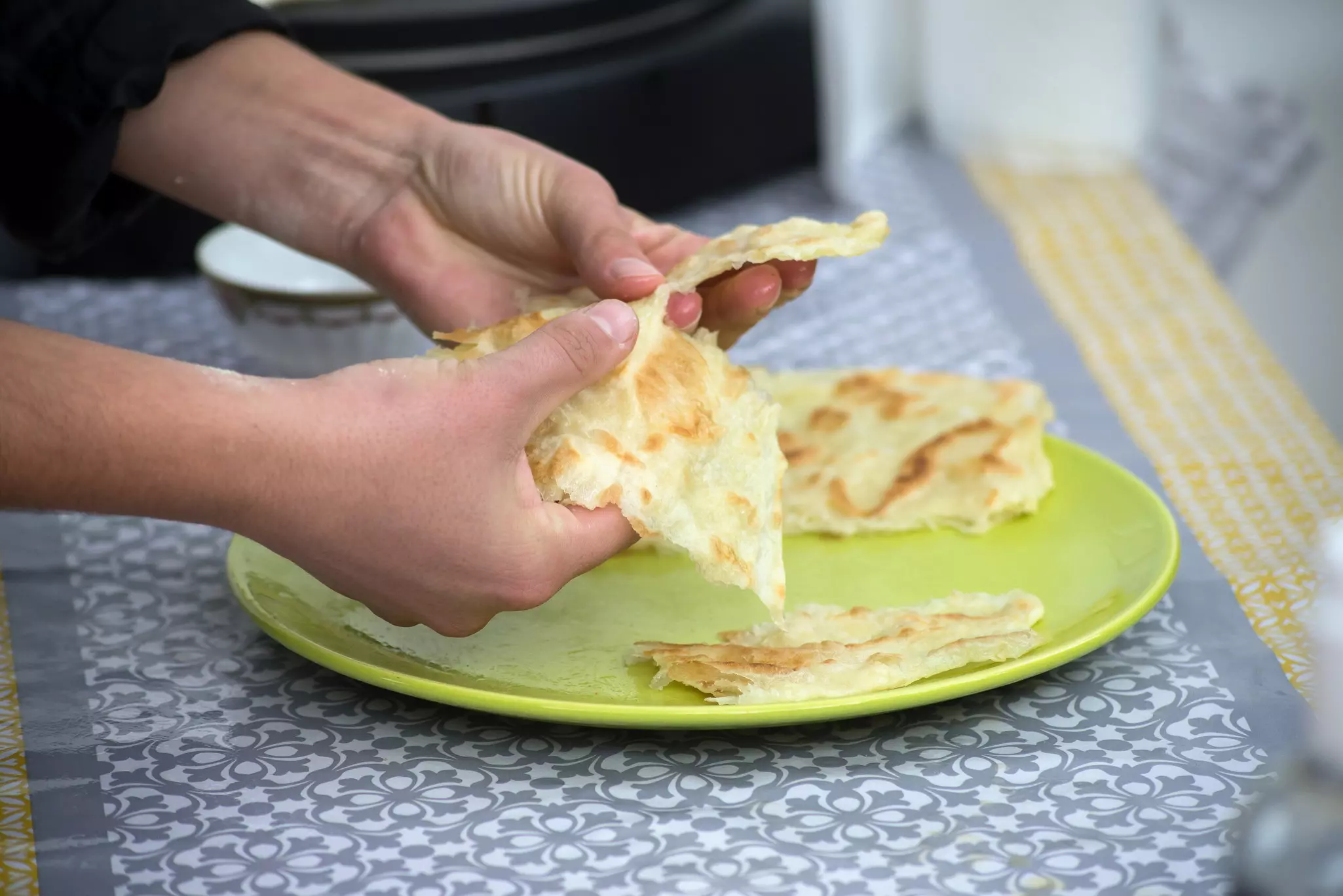 Hands preparing a flatbread made up of thin sheets of dough.