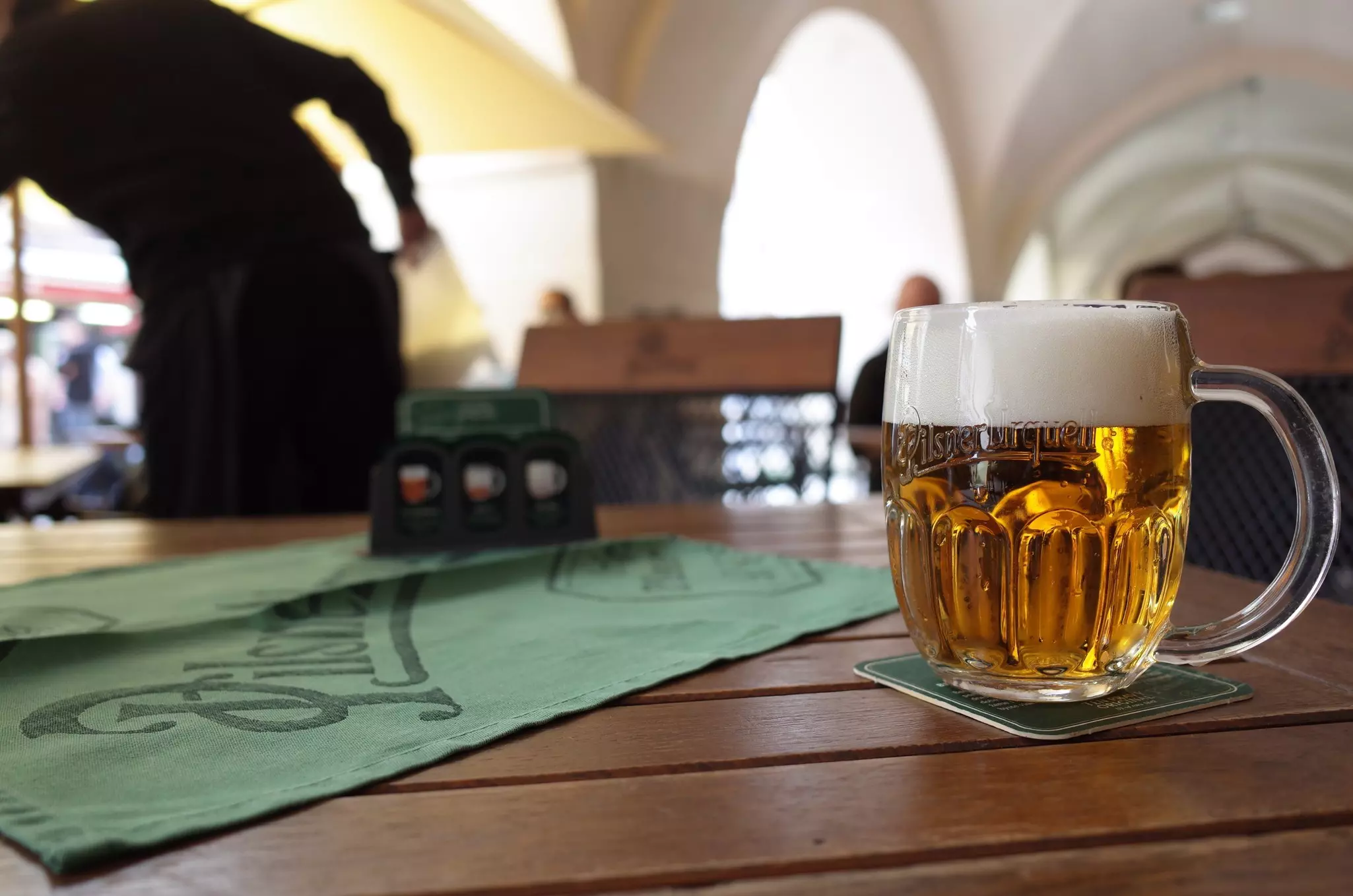 Glass of Czech-style Pilsner lager beer brewed by Pilsner Urquell on table of bar.
