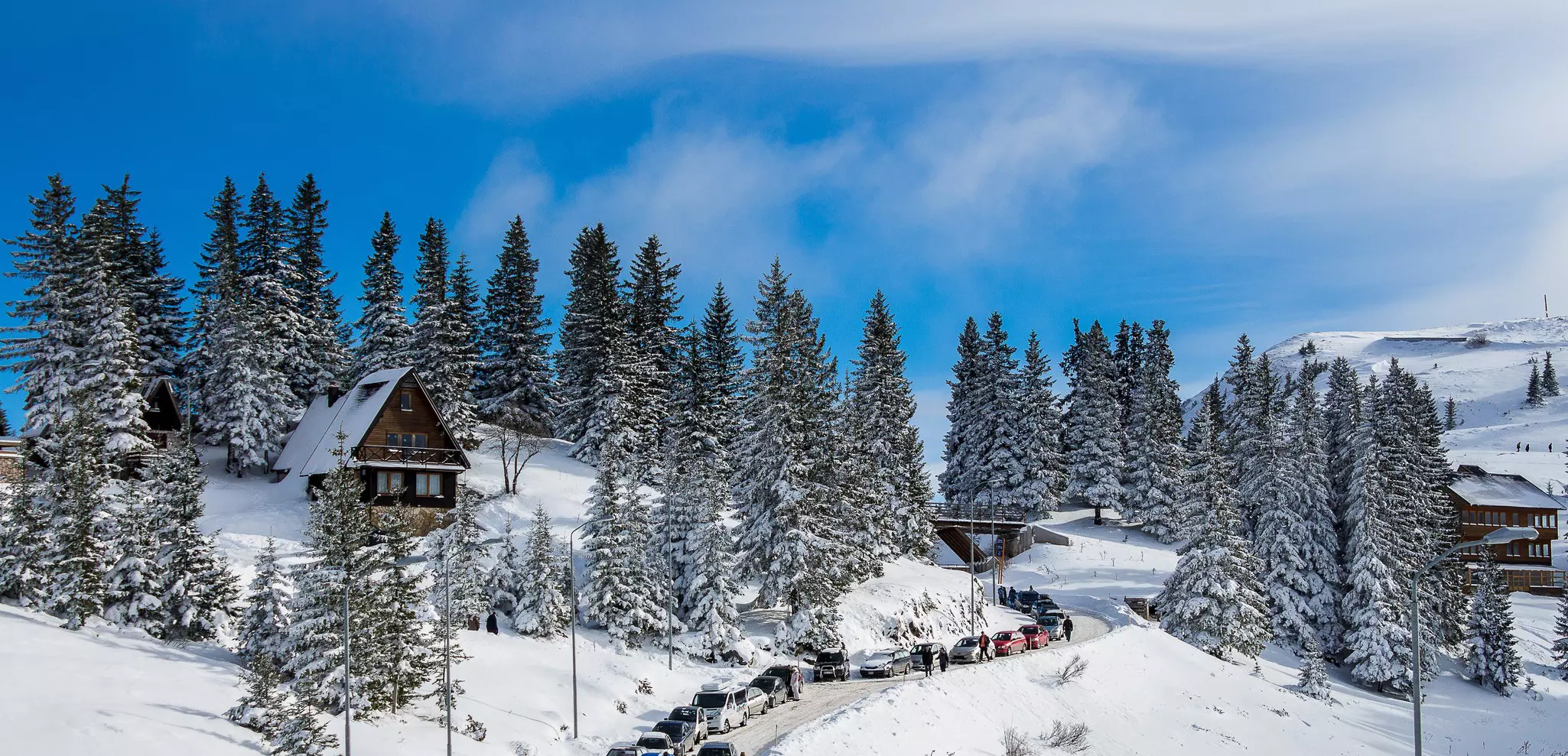 A mountainous settlement with trees, wooden chalets and the hillsides covered in thick snow.