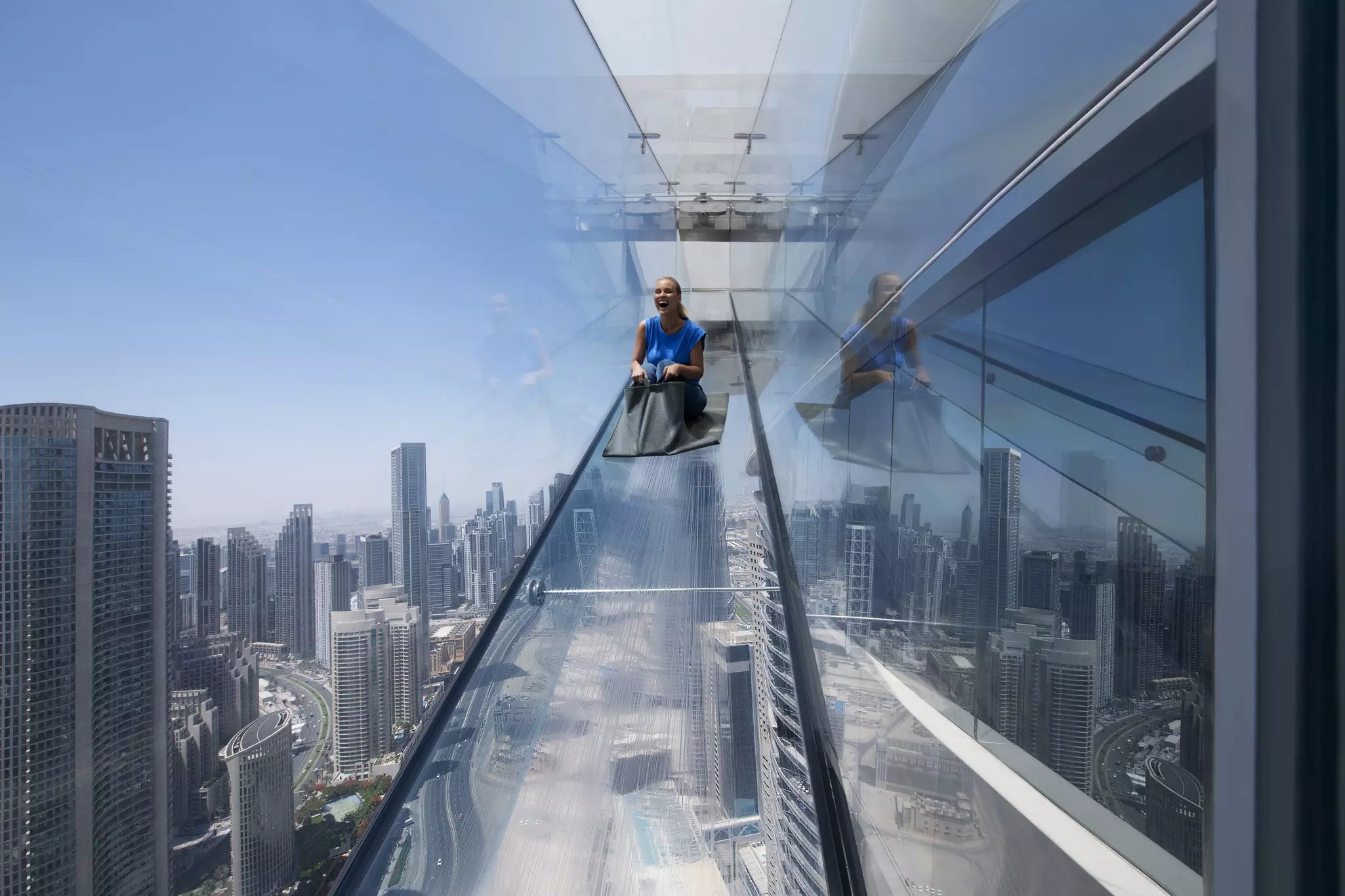 Woman going down a glass slide over the skyline of Dubai.