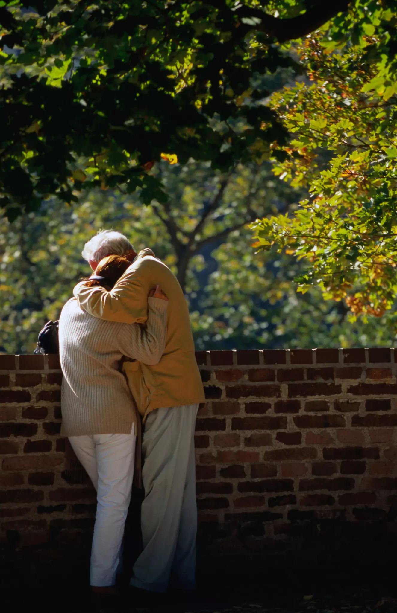 A couple hugging by a stone wall.