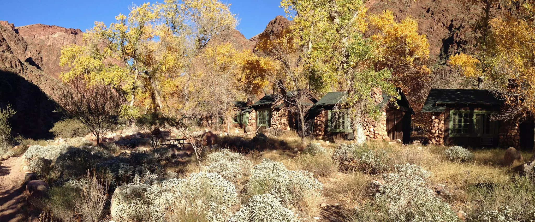 Stone cabins nestled among trees with red rock mountains in the background.