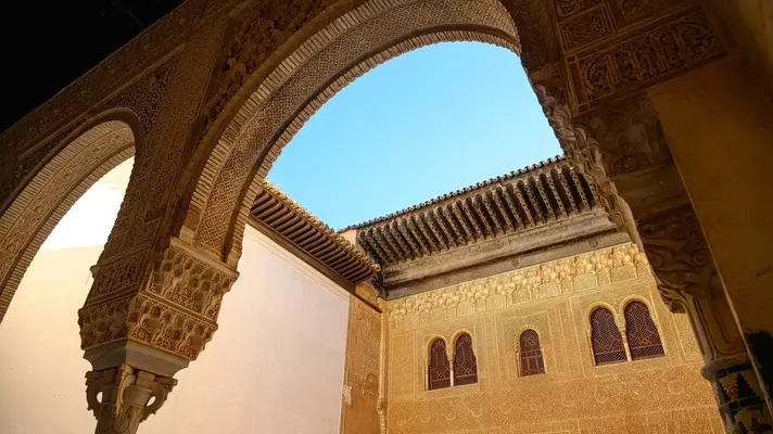Intricately carved Moorish arches and ceiling of the Alhambra with sunlight streaming through open rooftop