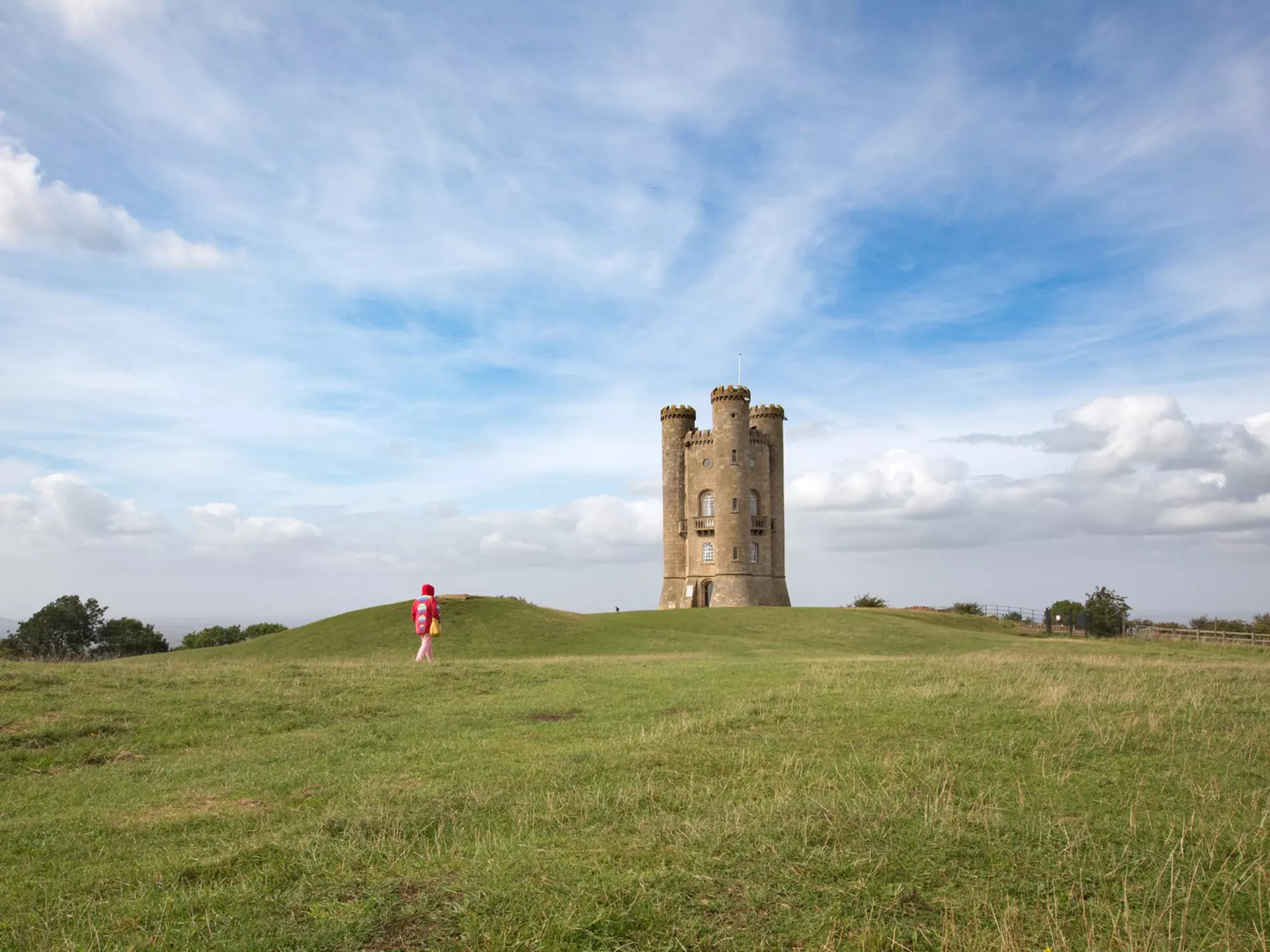 Woman in red walking toward the historic Broadway Tower, Broadway, Worcestershire, the Cotswolds, England, United Kingdom