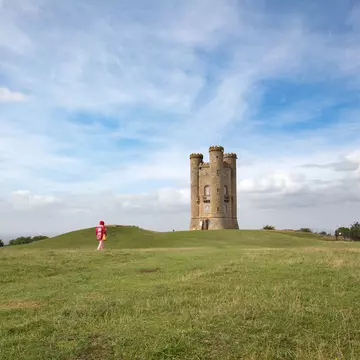 Woman in red walking toward the historic Broadway Tower, Broadway, Worcestershire, the Cotswolds, England, United Kingdom