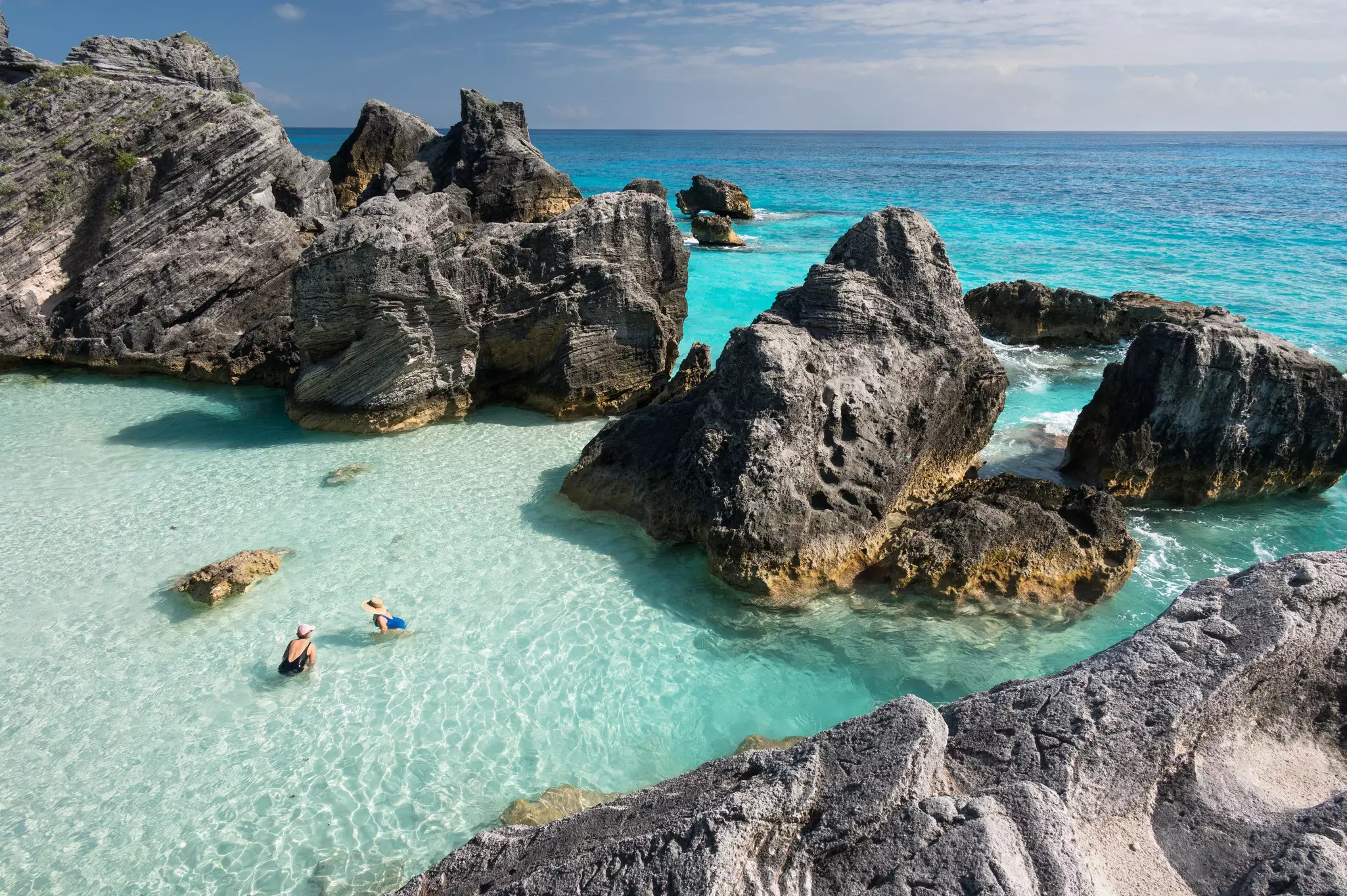 Aerial shot of two women in clear ocean water surrounded by large rocks.