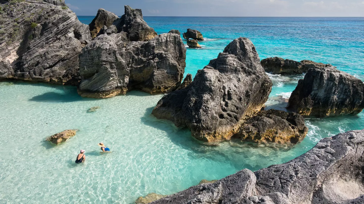 Aerial shot of two women in clear ocean water surrounded by large rocks.