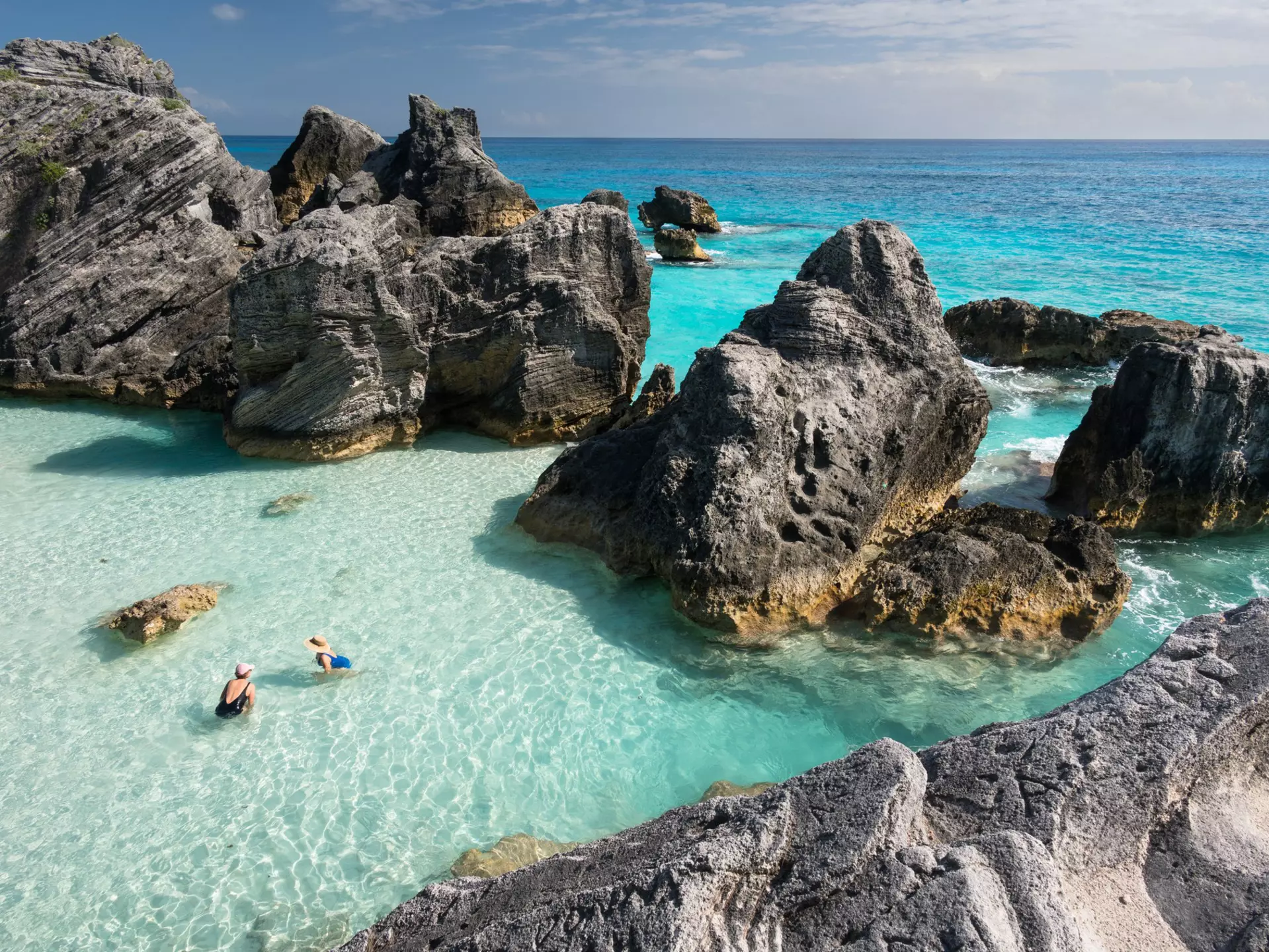 Aerial shot of two women in clear ocean water surrounded by large rocks.