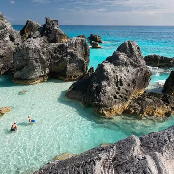 Aerial shot of two women in clear ocean water surrounded by large rocks.