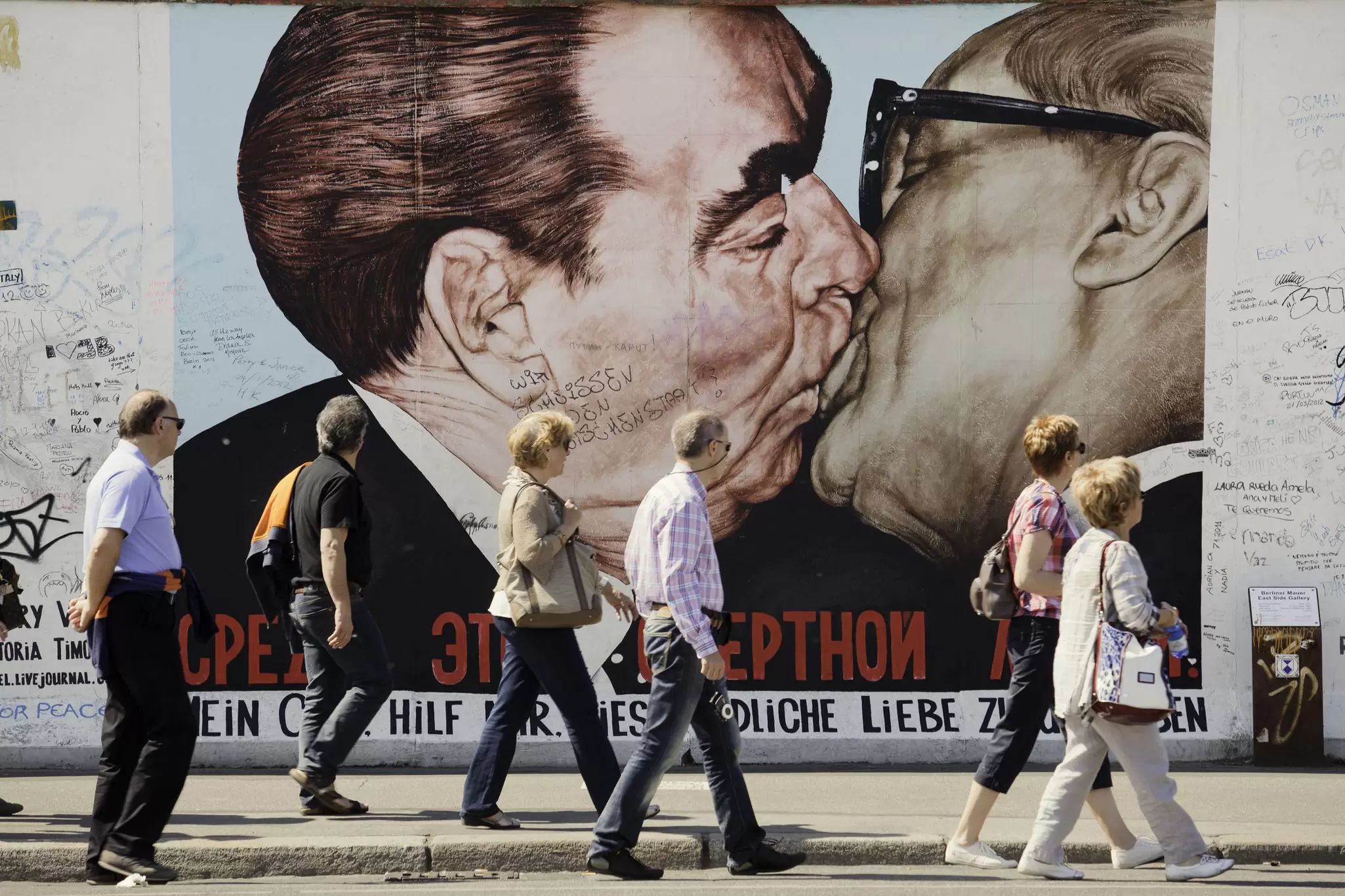 People walk past the 'My God, Help Me to Survive This Deadly Love' artwork on the East Side Gallery in Berlin. The artwork depicts a Russian and East German politician kissing.