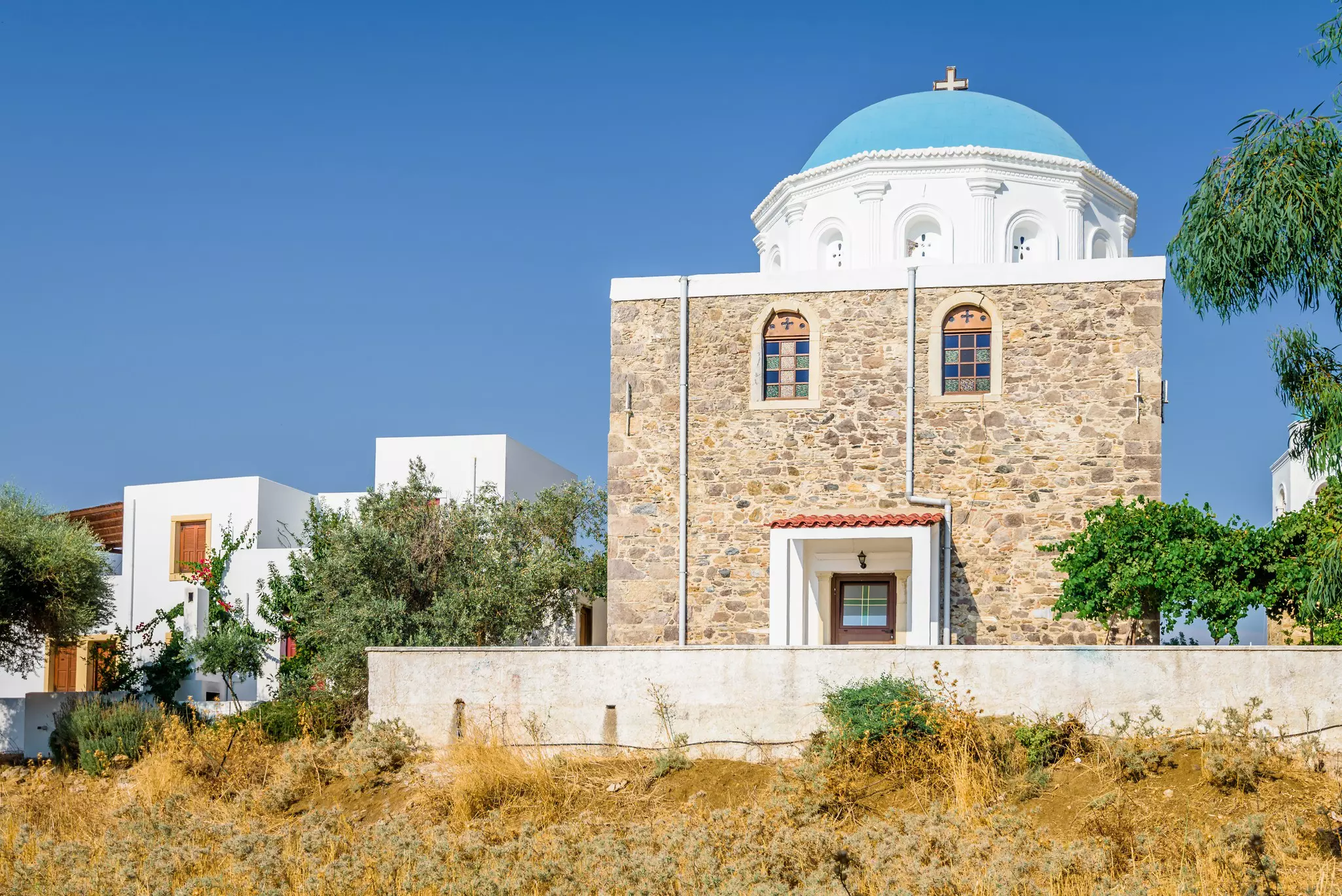 Holy greek stone church with white blue dome church in Evangelistra Asfendiou with cross over a blue sky.