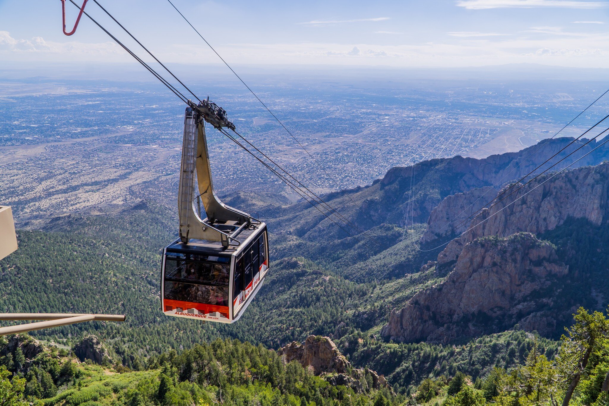 A cable car in mid-flight overlooking mountain scenery and wide, flat desert plains