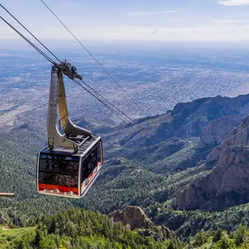 A cable car in mid-flight overlooking mountain scenery and wide, flat desert plains