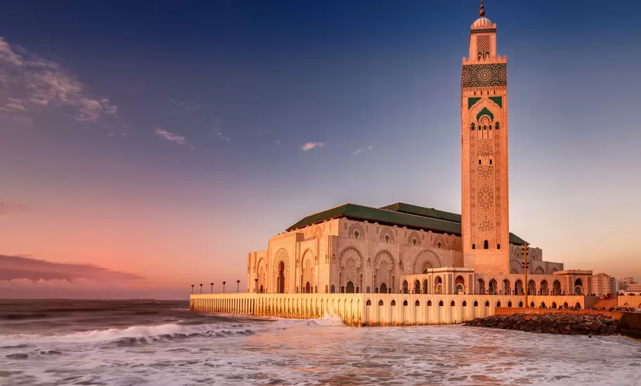 Hassan II Mosque and its tall minaret in Casablanca, on the Atlantic shore with waves breaking below at sunset