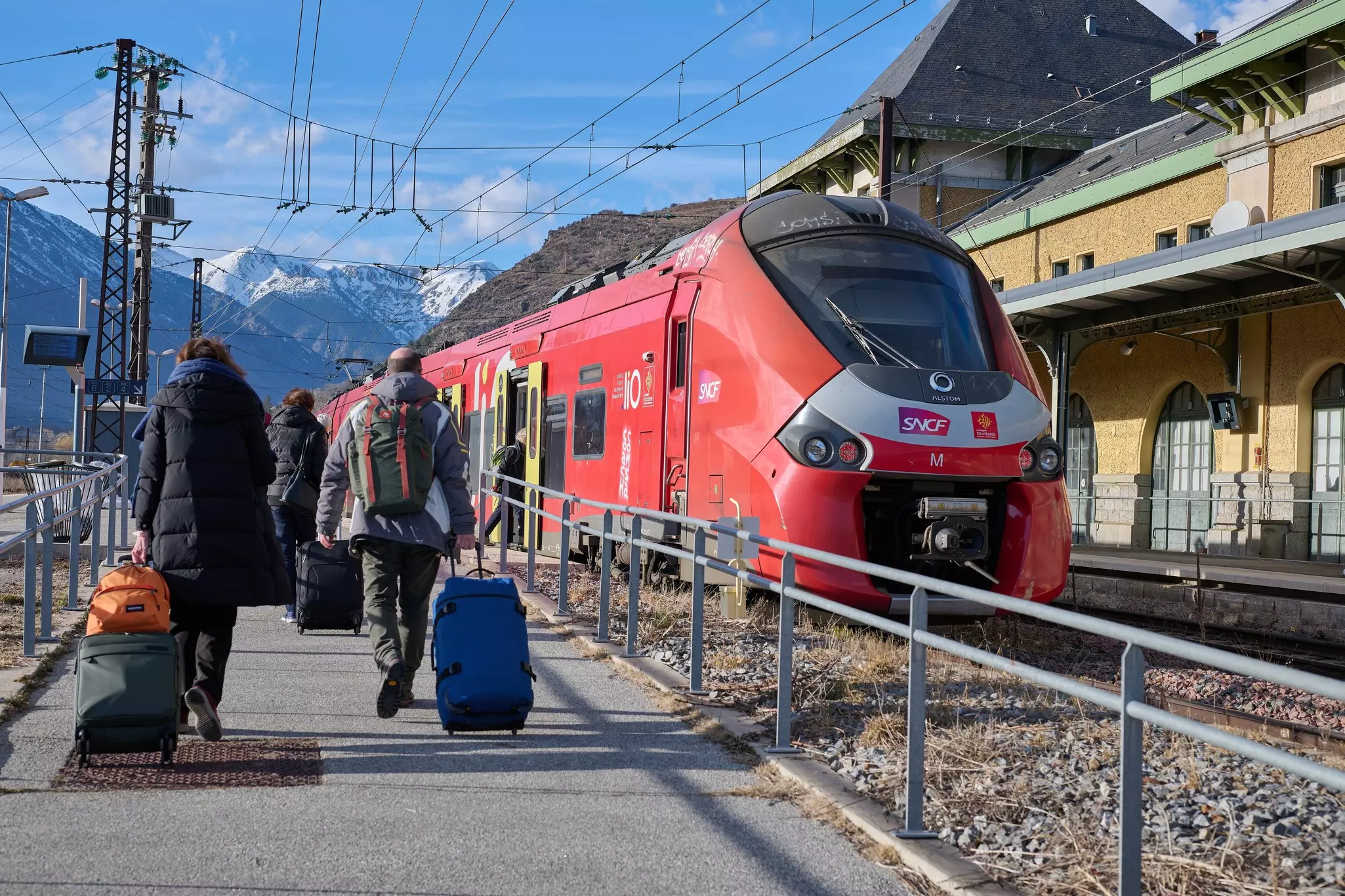People board the train in Latour-de-Carol train station in France, with the mountains behind.