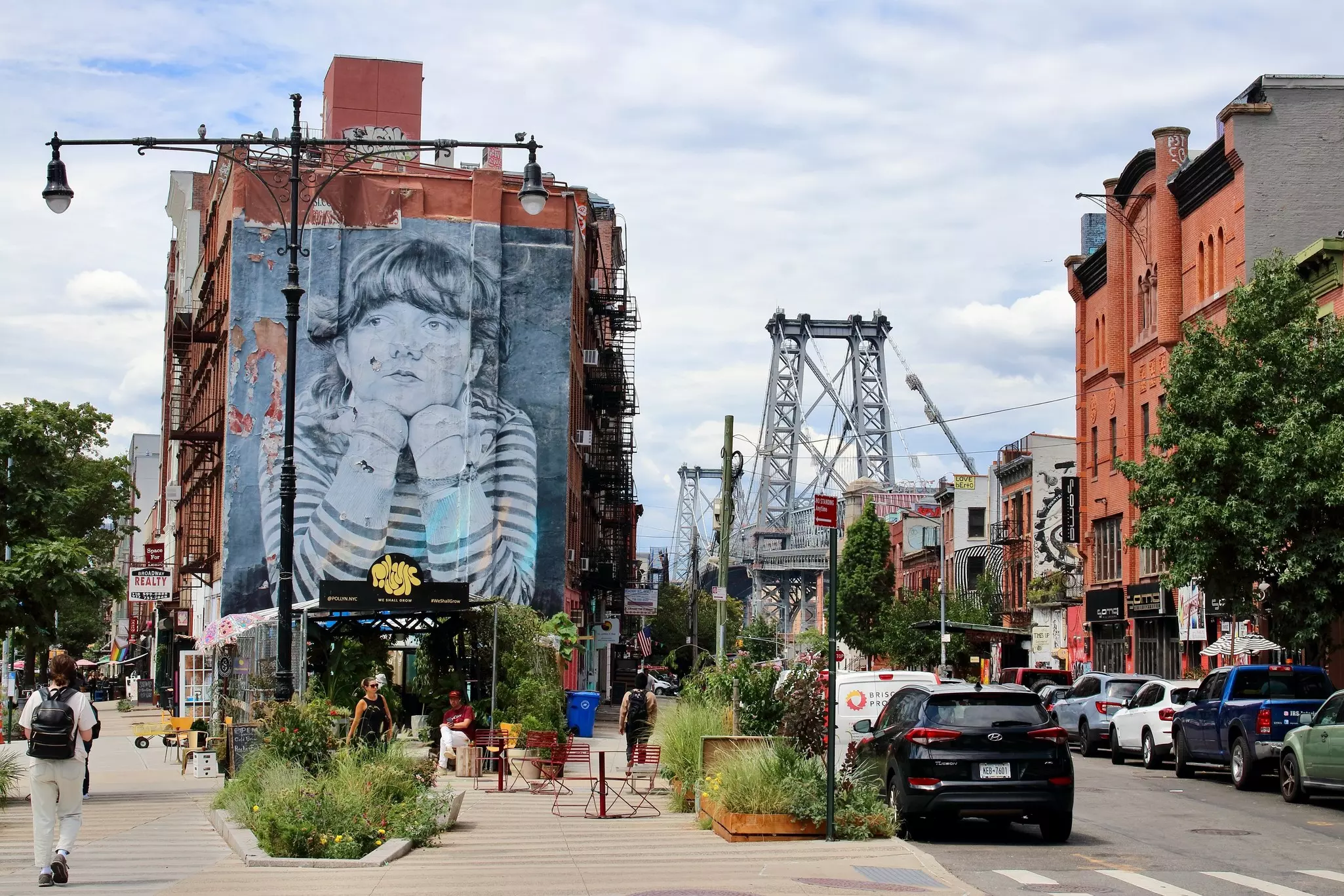 People walking toward a black and white mural of a child on the side of a building