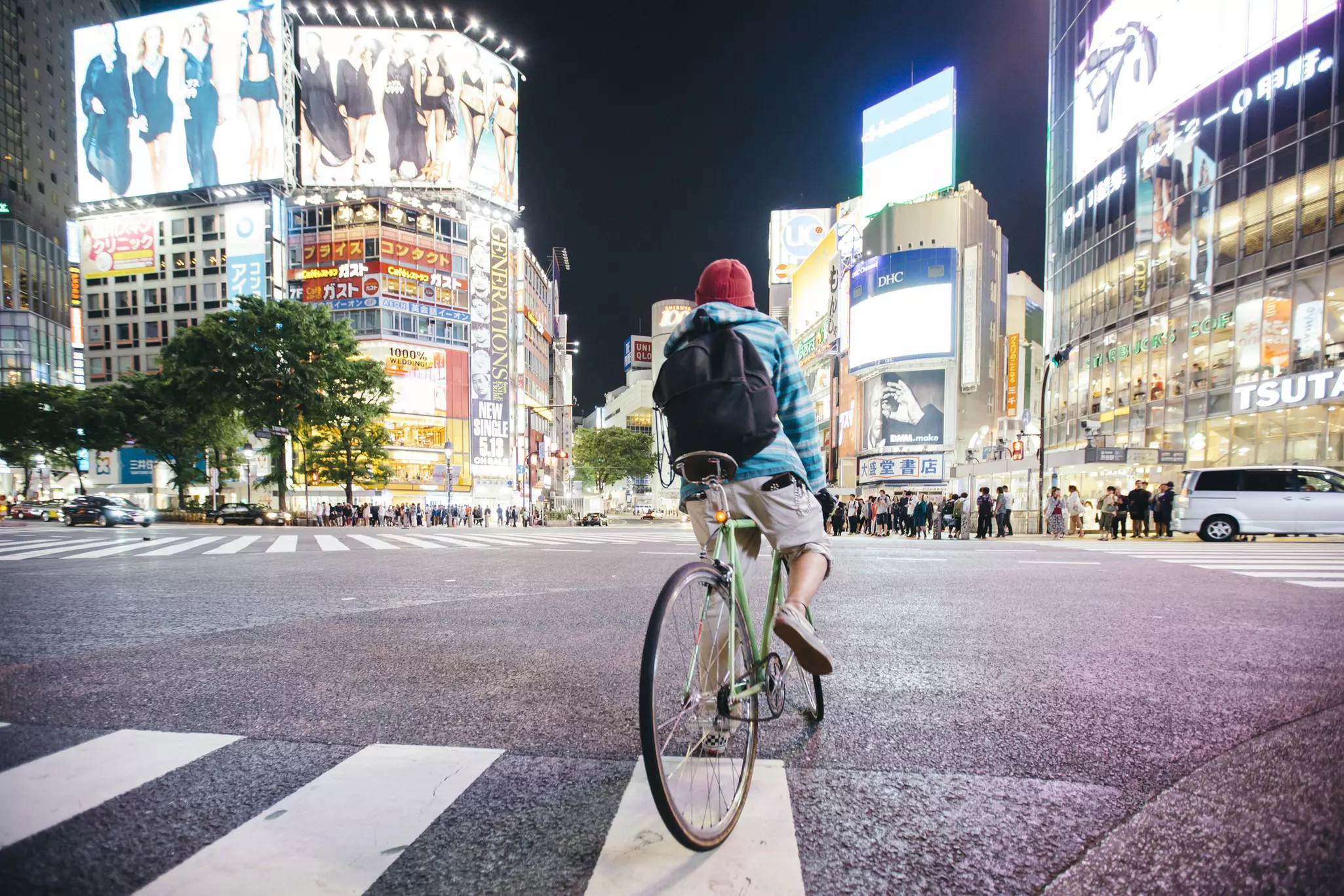 A cyclist wearing a backpack at a crosswalk in Tokyo at night.