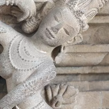 A weathered sandstone carving of a dancing figure displayed on a plinth.