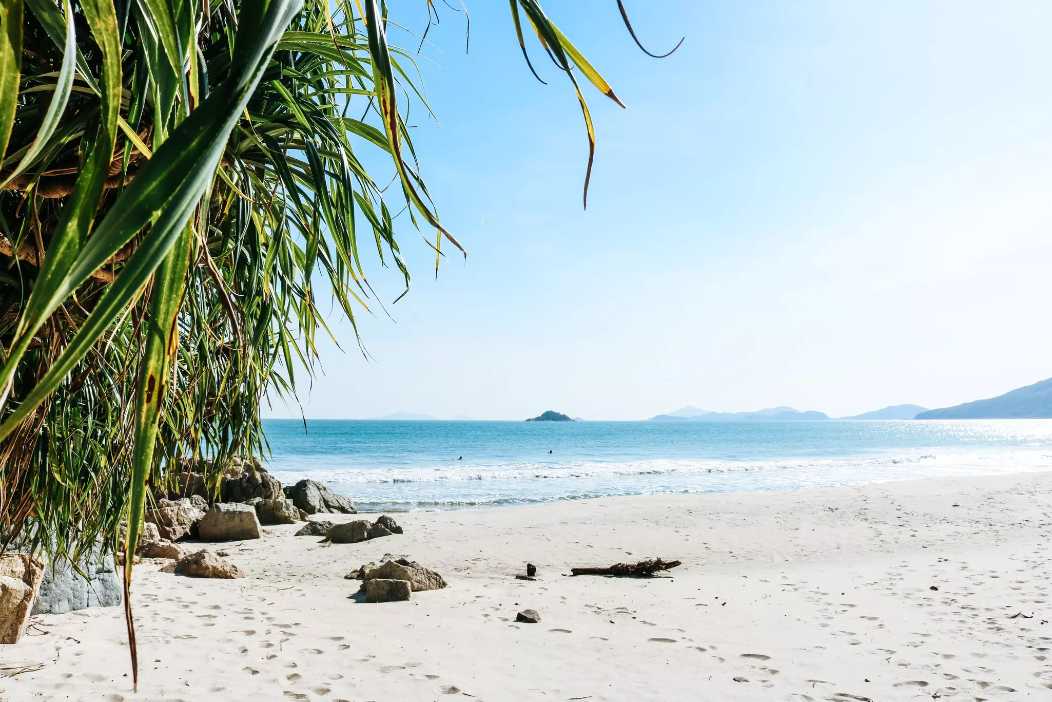 A tropical white-sand beach with an island out at sea in the distance